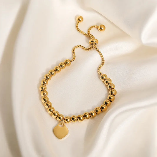 Pulsera de bolitas con dije de corazón, ajustable. Color dorado. Acero inoxidable.