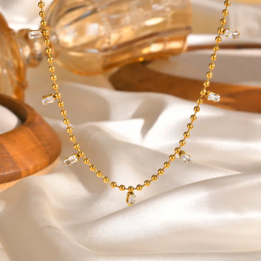 Collar de bolitas con circonias colgando. Color dorado. Acero inoxidable.