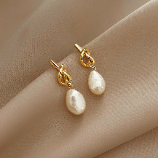 Aretes de nudo con perla colgando. Color dorado. Bisutería.