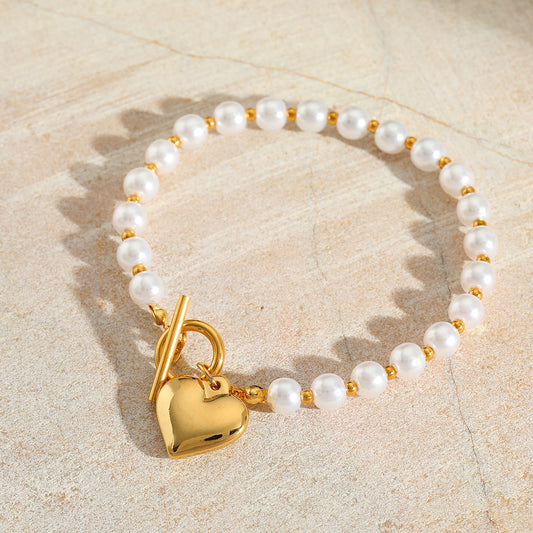 Pulsera perla con dije de corazón. Color dorado. Acero inoxidable.