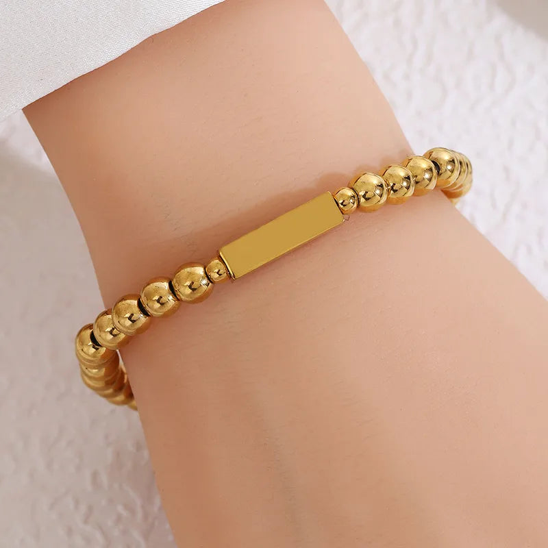 Pulsera bolitas con dije rectangular. Color dorado. Acero inoxidable.